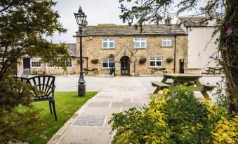 a traditional stone building with a sign , surrounded by greenery and outdoor seating area with umbrellas at The Sawley Arms