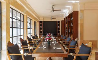 A spacious room with a long table and chairs positioned in the center, adjacent to an unoccupied book at Amanbagh