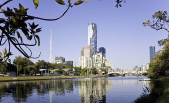 a city skyline with a river in the foreground and tall buildings in the background at Ibis Melbourne Hotel and Apartments