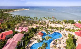 aerial view of a resort with a large pool surrounded by palm trees , beach chairs , and a hotel at Bahia Principe Grand la Romana - All Inclusive
