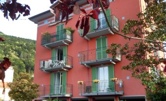 a three - story red and green building with balconies , surrounded by trees and flowers , on a sunny day at Franco