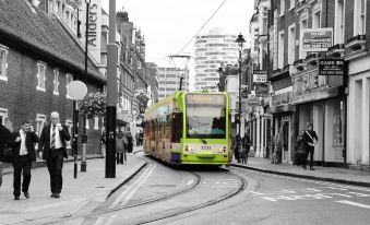 a green trolley bus is driving down a city street , surrounded by buildings and pedestrians at Lansdowne Hotel