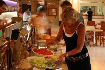 a woman in a black dress is standing at a buffet table , preparing food for a crowd of people at Valley Village