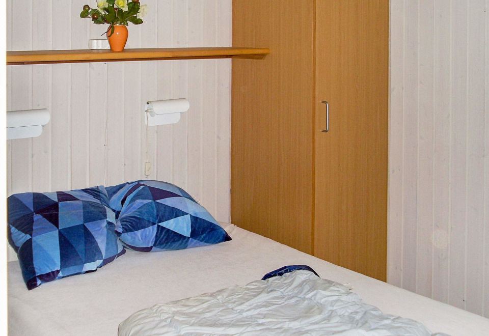 a bed with blue and white pillows is in a room with wooden walls and a shelf holding flowers at Hvidbjerg