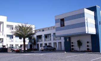 a white building with blue stripes , surrounded by palm trees and a parking lot filled with cars at Lotus Boutique Inn and Suites