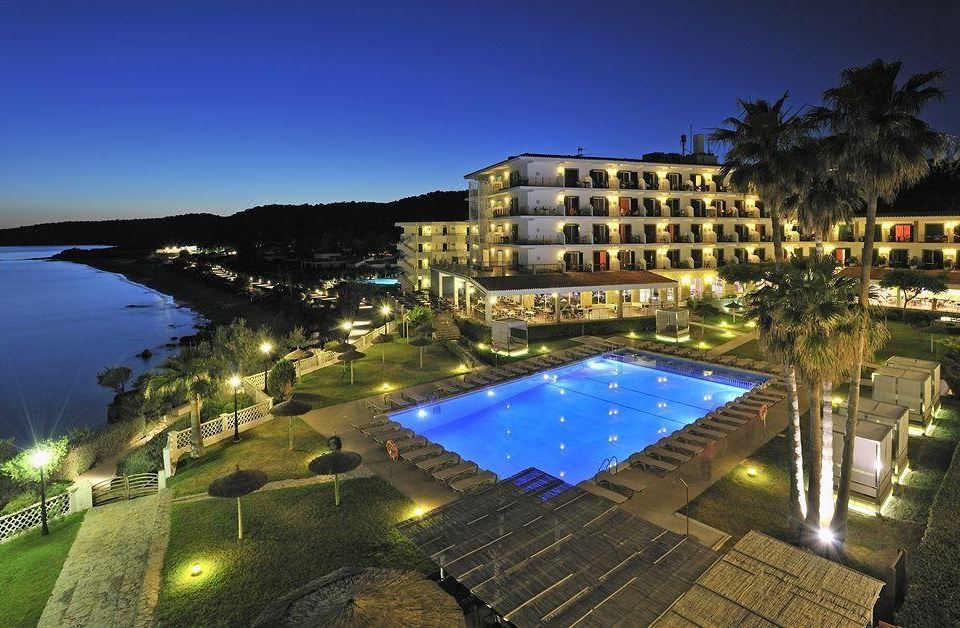 a large hotel with a swimming pool surrounded by palm trees at night , illuminated by lights at Villa Le Blanc Gran Melia