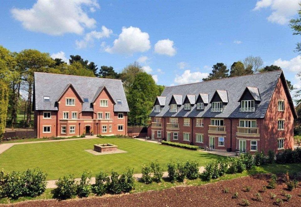 a large brick building surrounded by grass and trees , with a fountain in the foreground at Rockliffe Hall Hotel Golf & Spa