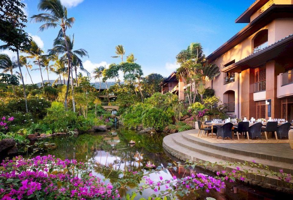 a beautiful tropical garden with lush greenery , flowers , and a pond where people are sitting at outdoor tables at Four Seasons Resort Lana'i