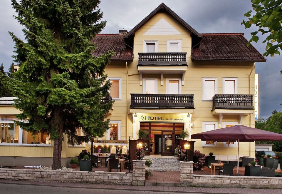 a large yellow hotel building with a red roof and a tree in front of it at Hotel am Kurpark