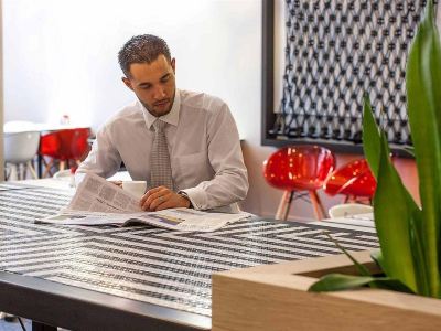 a man in a white shirt is sitting at a table with a book , looking at the table with various items on it at Ibis Melbourne Hotel and Apartments