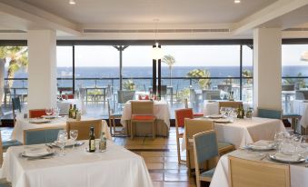 a large dining room with white tablecloths and chairs is shown with a view of the ocean at Parador de Mojacar