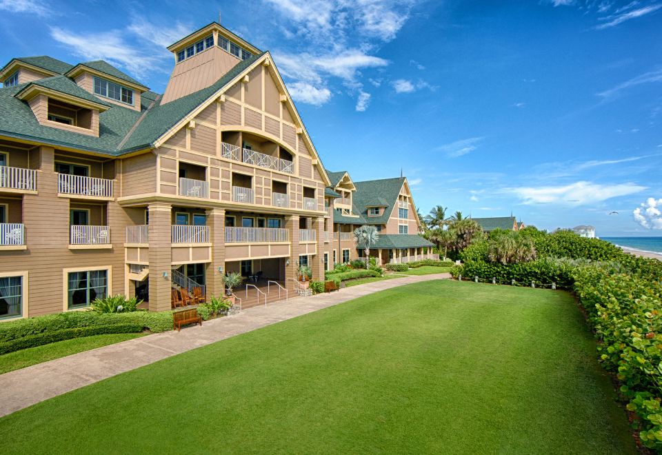 a large building with a green lawn in front of it and palm trees behind at Disney's Vero Beach Resort