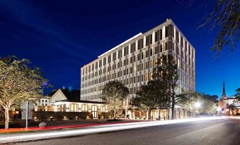 a large , modern building with multiple floors and balconies , lit up at night , surrounded by trees and cars passing by at The Dewberry Charleston