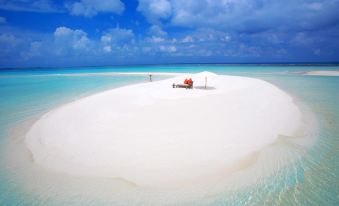 a man sitting on a white sandy island in the ocean , surrounded by clear blue water at Sunshine Lodge