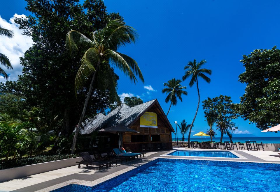 a tropical resort with a swimming pool , palm trees , and a blue sky , under a clear sky at Berjaya Beau Vallon Bay Resort & Casino