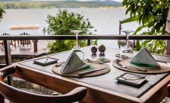 a wooden dining table set with plates , glasses , and napkins on a balcony overlooking a body of water at Jicaro Island Lodge Member of the Cayuga Collection