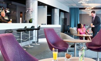 a modern lounge area with purple chairs and tables , a bar area , and two people at Mercure Paris Ivry Quai de Seine