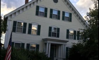 a large white house with green shutters and a flagpole in front of it , under a cloudy sky at Gibson House