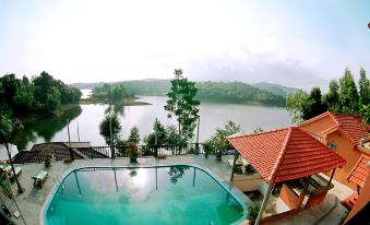 a large swimming pool is surrounded by trees and a building , with a lake in the background at Phong Nha Lake House Resort