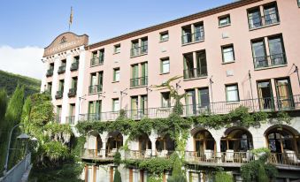 a large building with a pink facade and balconies is surrounded by greenery , and water in front of it at Le Grand Hôtel