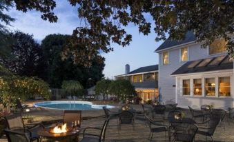 a well - lit outdoor area with tables and chairs , a fire pit , and a swimming pool , under the glow of dusk at The Jacqueline House of Wilmington