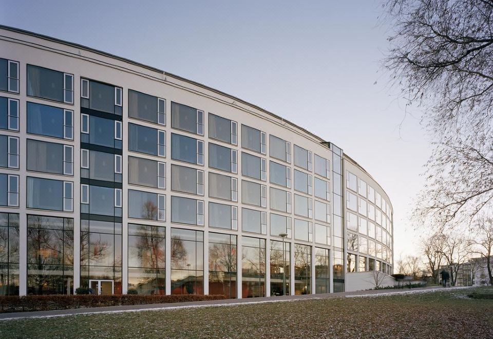 a modern building with large windows and a curved roof , surrounded by grass and trees at Scandic Linköping City