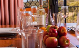 a dining table with a bottle of wine , a wine glass , and various fruits , creating an inviting atmosphere for a meal at Nutkin Lodge