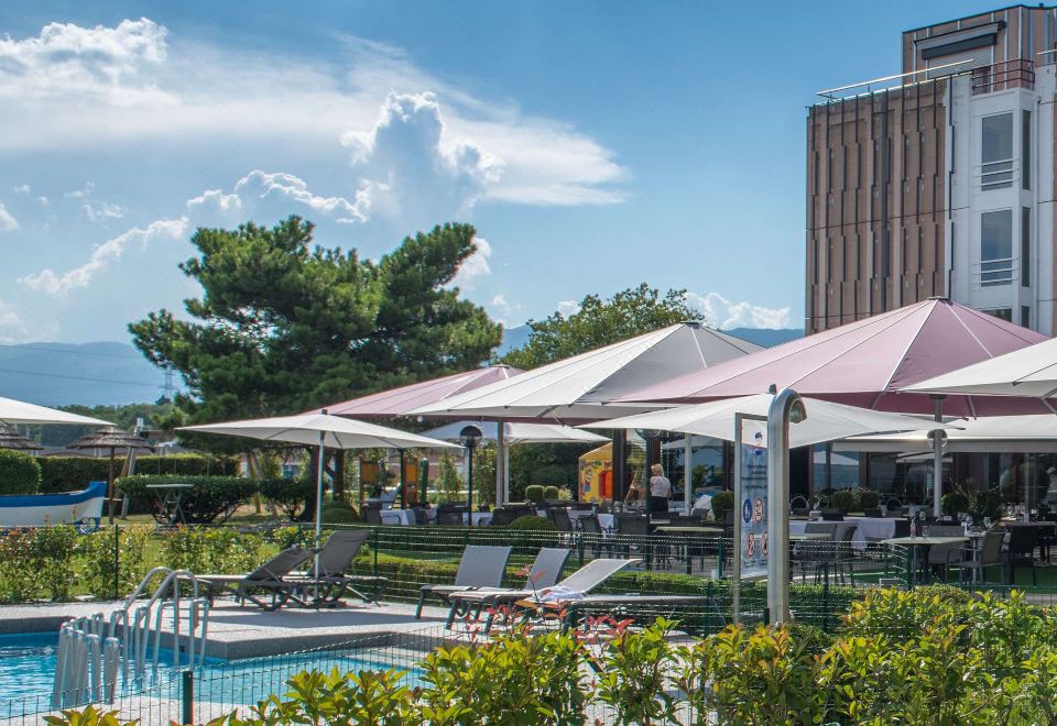 a patio area with tables , chairs , and umbrellas surrounding a pool , providing shade and comfort for people to enjoy at Everness Hotel & Resort