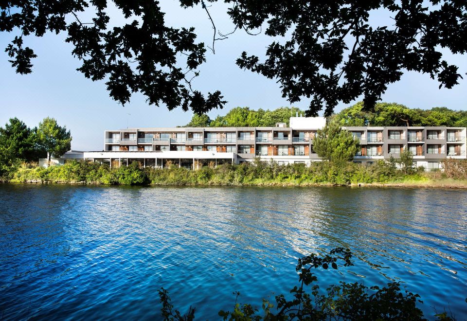 a large building surrounded by trees and a body of water , creating a picturesque scene at Best Western Plus Hotel les Rives du Ter