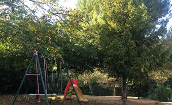 a colorful playground with swings and a slide is situated in a wooded area under the shade of trees at Le Bellevue