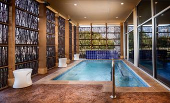 a modern indoor pool with a spa section and a unique design of stone walls at GLo Best Western DeSoto Dallas