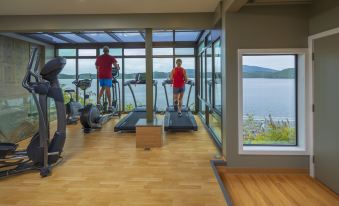 a gym with wooden floors and large windows overlooking a body of water , with people working out on treadmills at Crest Hotel