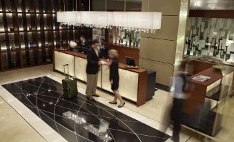 a hotel lobby with a reception desk and several people , some of whom are wearing suits and ties at Montreal Airport Marriott in-Terminal Hotel