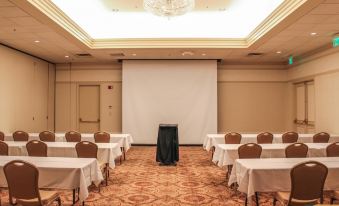 a large , empty conference room with multiple tables and chairs , a projector screen , and a chandelier at General Morgan Inn