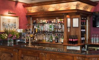 a well - stocked bar with various bottles and glasses on the counter , along with a wine glass and a bottle of beer at Berjaya Eden Park London Hotel