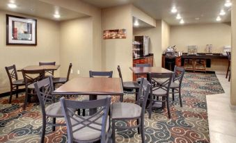 a dining area with several tables and chairs , as well as a coffee station in the background at Cobblestone Hotel & Suites - Erie