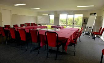 a conference room with a red table and chairs , white walls , and large windows , ready for meetings or presentations at Sanctuary Inn on Westernport