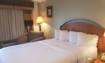 a large bed with white sheets and pillows is in a room next to a chair and lamp at White Columns Inn