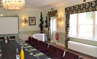a conference room with a long table , multiple chairs , and curtains , decorated with various items such as bottles and vases at Beechfield House