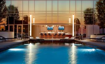 a modern hotel with a large outdoor pool area , bar , and dining area at dusk at Omni Frisco-Dallas Hotel at the Star