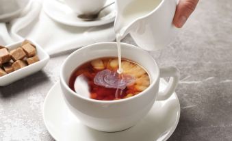 a person is pouring milk into a cup of tea on a dining table , accompanied by other cups and bowls at Seabird Lodge Fort Bragg