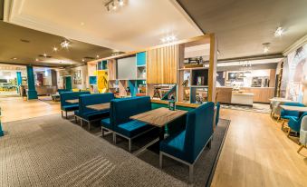 a modern hotel lobby with blue seating , wooden tables , and a large screen on the wall at Holiday Inn Leeds - Brighouse