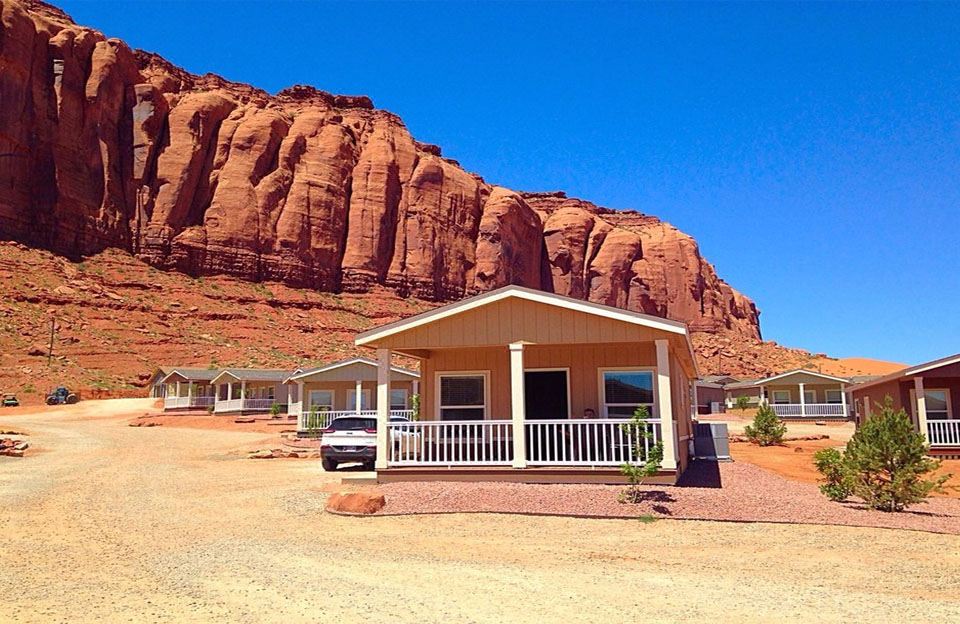 a small wooden house with a porch is situated in front of a red rock cliff at Goulding's Lodge