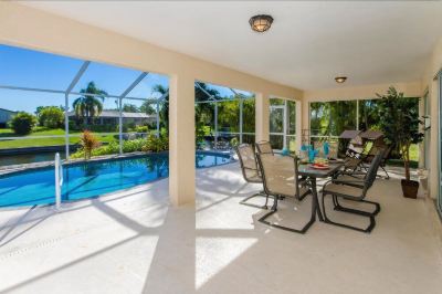 a large outdoor patio with a dining table and chairs , overlooking a pool area surrounded by palm trees at Italy