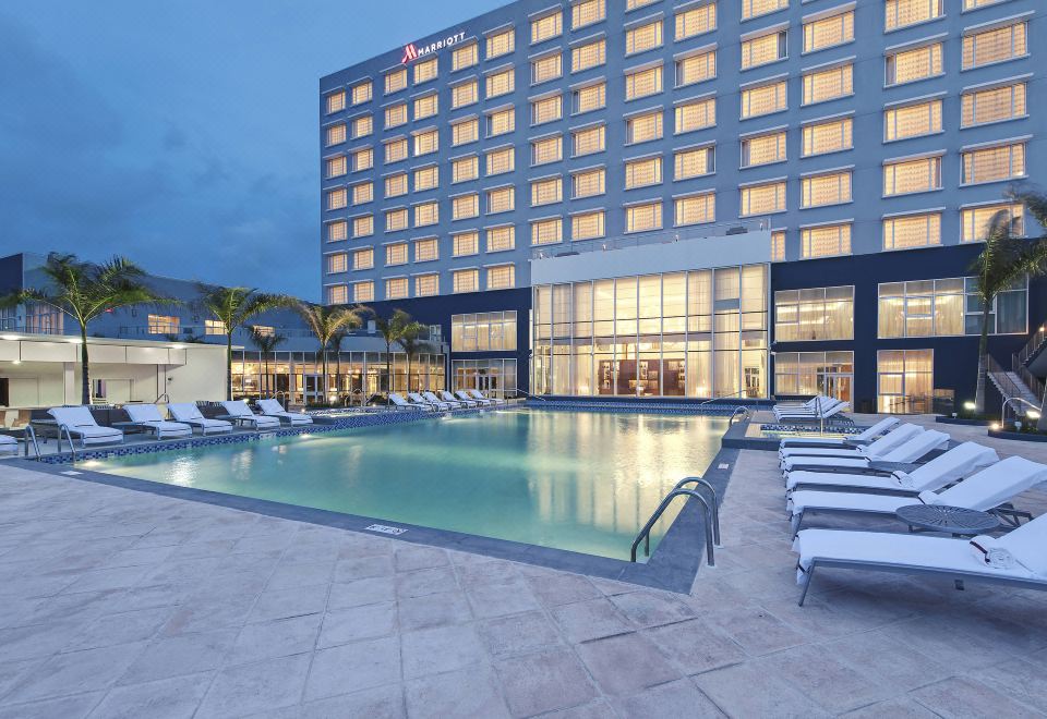 a large hotel with a swimming pool and sun loungers in front of it at dusk at Guyana Marriott Hotel Georgetown