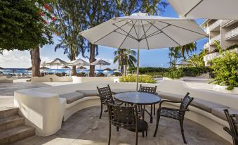 a patio with a table and chairs under an umbrella , surrounded by palm trees and ocean views at Bougainvillea Barbados