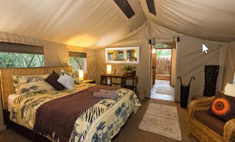 a cozy bedroom with a bed , a door , and a chair in a tent - like room at Tembe Elephant Park
