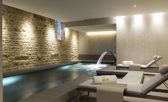 a modern spa with a stone wall , two jacuzzi areas , and white towels on the floor at Chateau de Bagnols