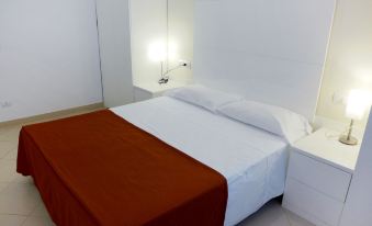 a clean , well - organized bedroom with a white bed , a red comforter , and a lamp on the nightstand at Nautilus