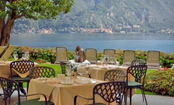 a restaurant with tables set up on the terrace , offering a view of the lake and mountains in the background at Grand Hotel Menaggio
